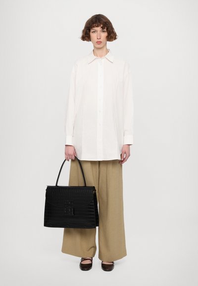 Borsa in pelle di cocodrillo nera con chiusura a patta, abbinata a una camicia bianca a bottoni e pantaloni beige a gamba larga.