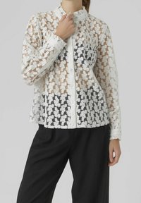 Chemise transparente blanche à motifs floraux avec col et boutons, dotée de poignets à volants et d'un dégradé du blanc au noir en bas.