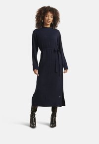 Vestito in maglia blu navy con motivo testurizzato, maniche lunghe, vita con cintura e spacco laterale, abbinato a stivali neri al ginocchio.