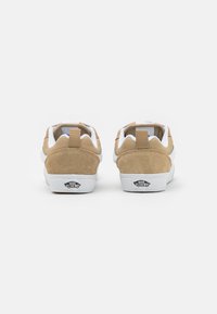Brown suede sneakers with white accents, a padded collar, and a rear pull tab. Features classic Vans logo on the heel and textured sole.