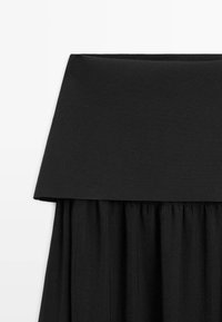 Haut noir à épaules dénudées avec un large col plié et un tissu froncé sous la ligne de poitrine.