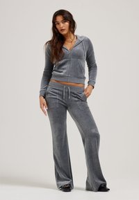 Grauer, Reißverschluss-Hoodie mit Fronttaschen, kombiniert mit passenden weit geschnittenen Hosen. Hergestellt aus einem weichen, strukturierten Stoff für Komfort und Bewegungsfreiheit.