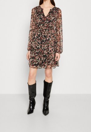 Schwarzes, transparentes Kleid mit Blumenmuster, langen Ärmeln und V-Ausschnitt. Mit einer taillierten Taille und einem ausladenden Rock versehen. Schwarze kniehohe Stiefel.