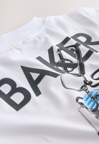 Baltas audinys su juodu užrašu „BAKER“ bei atspausdintu alpinizmo įrangos, įskaitant karabinus ir diržus, dizainu.