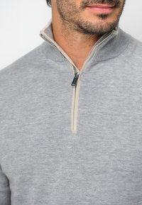Grauer Zip-Pullover mit einem kontrastierenden beigen Kragenbesatz. Verfügt über einen gerippten Hals- und Ärmelbund, hergestellt aus glattem Strickstoff.