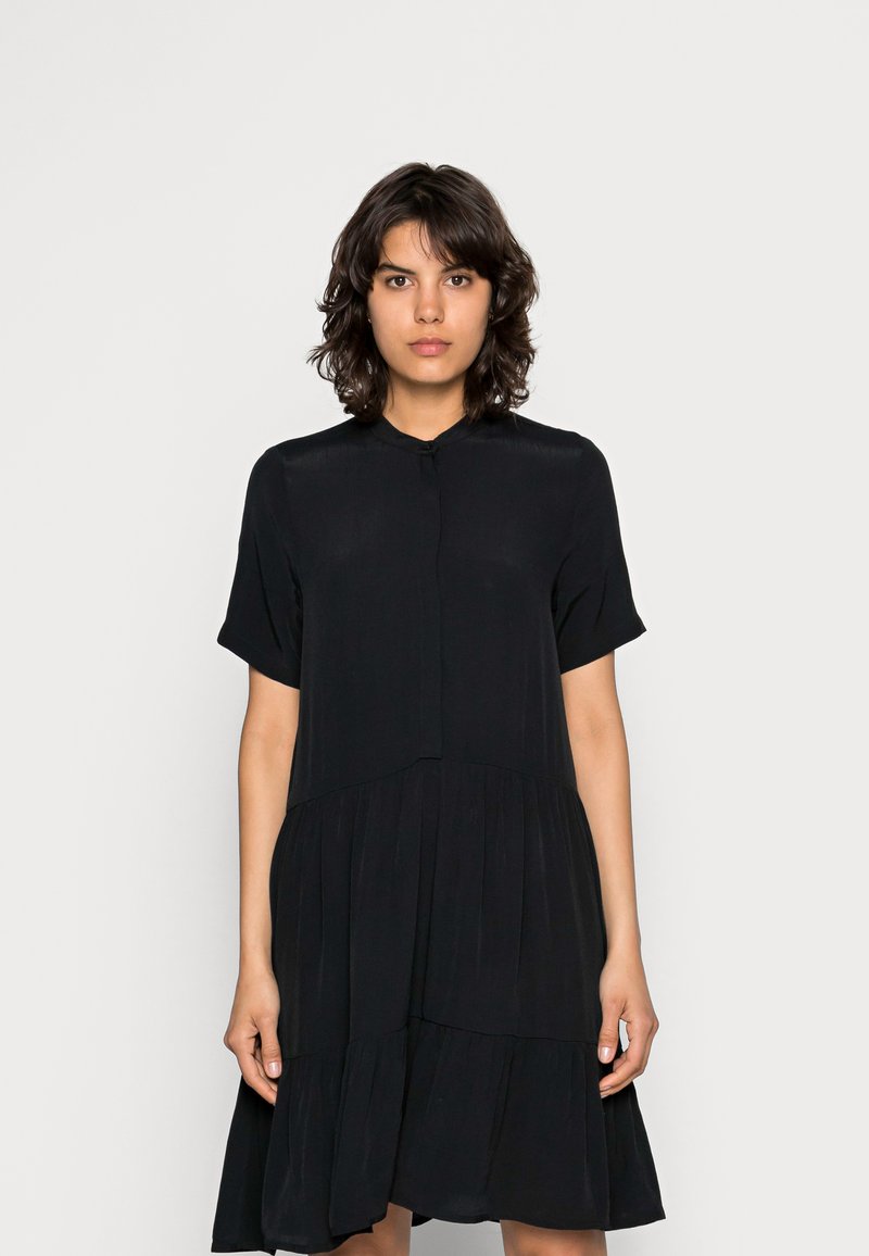 Vestido preto feito de tecido leve, apresentando um decote alto, mangas curtas e um design em camadas com uma silhueta fluida.