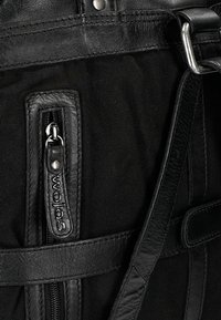 Borsa nera caratterizzata da un mix di tela testurizzata e pelle, con tasca zip e dettagli in pelle, inclusi un'etichetta con il logo e una tracolla regolabile.