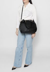 Borsa a mano in pelle nera con doppie maniglie e tracolla lunga regolabile. Texture liscia, forma arrotondata e dettagli in metallo argento.