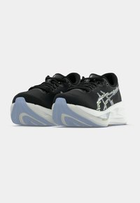 Chaussures de sport noires avec une tige en tissu texturé, présentant des accents réfléchissants, une semelle intermédiaire blanche rembourrée et une semelle extérieure en caoutchouc bleue.