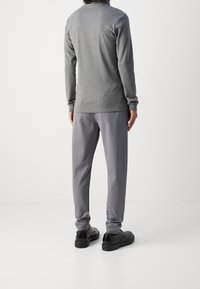 Grau langärmliges Hemd, kombiniert mit grauen schmal gestreiften Hosen. Das Outfit hat ein schlichtes Design und wird von schwarzer Fußbekleidung ergänzt.