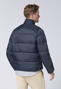 Navyblauer Puffer-Jacke mit hohem Kragen, gepolstertem Design und glatter Textur. Das Kleidungsstück verfügt über horizontale Nähte für zusätzliche Isolierung.
