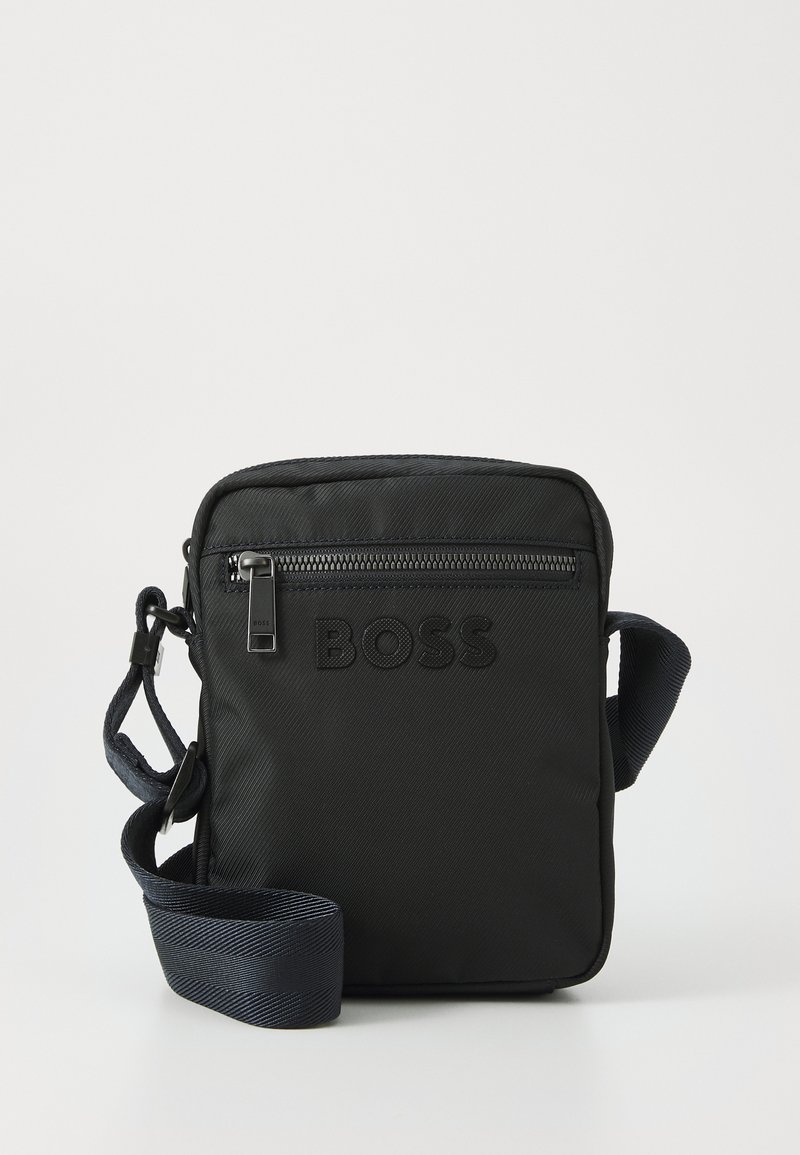 Black nylon crossbody bag with embossed logo, horizontal zip pocket, and a textured adjustable shoulder strap. Square-shaped design.