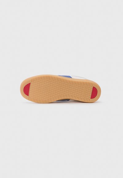 Hvit sneakersåle med en teksturert beige gummibase, med et rødt aksentfarge på hælen og en blå stripe langs siden.