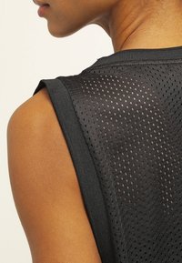 Czarny bezrękawnik sportowy wykonany z siateczkowego materiału, z teksturowaną powierzchnią i małymi otworami oraz wzmocnioną linią dekoltu.
