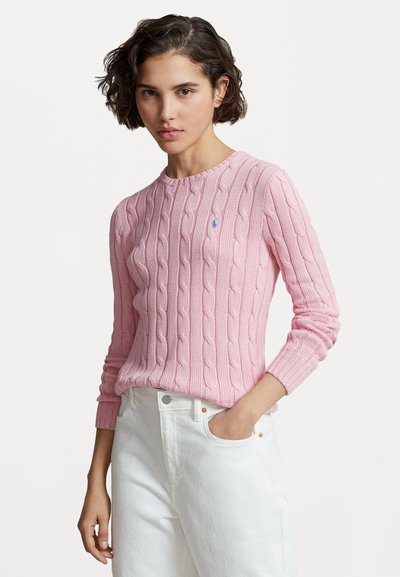 Pull en maille torsadée rose clair avec un col rond et des poignets côtelés. Détail de petit logo sur la poitrine. Associé à un jean blanc.