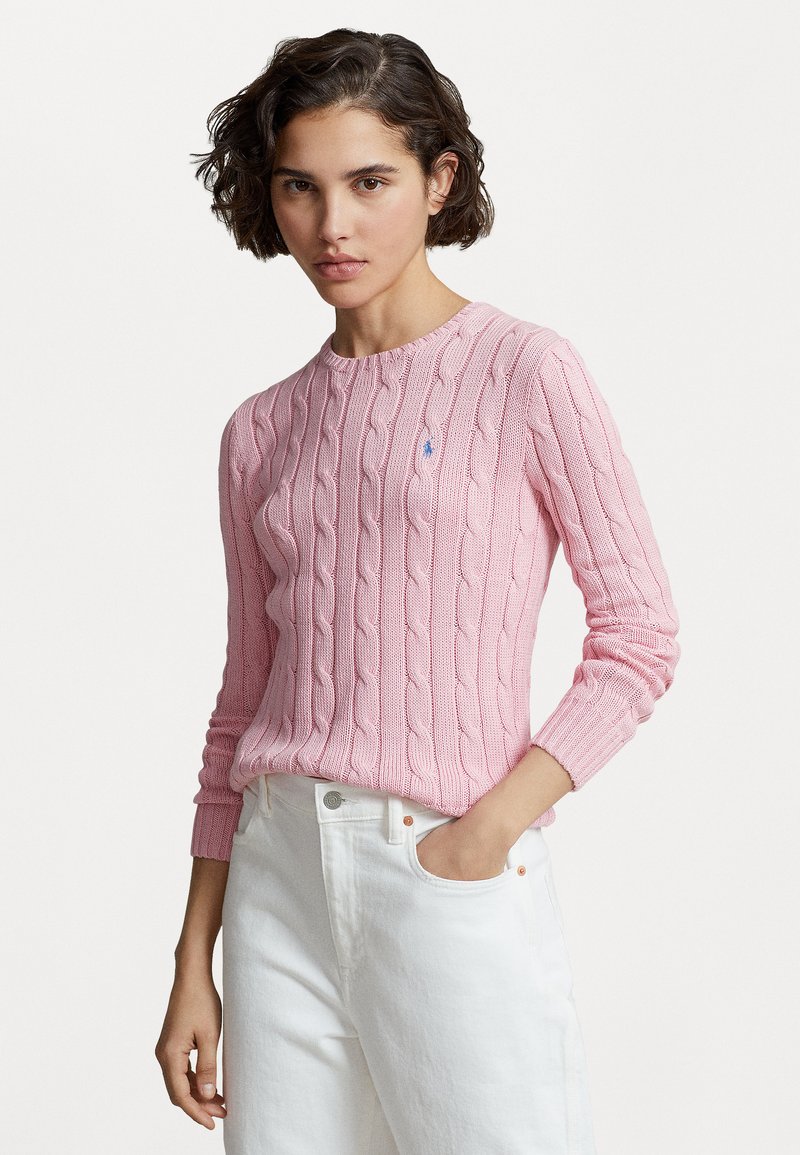 Pull en maille torsadée rose clair avec un col rond et des poignets côtelés. Détail de petit logo sur la poitrine. Associé à un jean blanc.