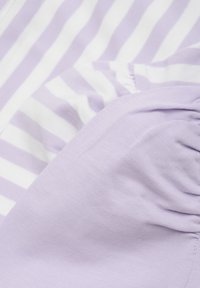 Ljust lila bomullstyg med vita vertikala ränder, med en ihopkrupen textur och slät yta. Fokus på överlappningen av olika tygsektioner.