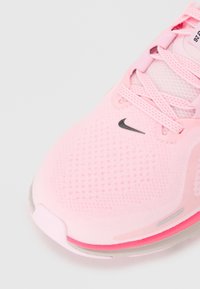 Ροζ αθλητικό παπούτσι με αναπνεύσιμο πλέγμα επάνω, στρογγυλή μύτη, λεπτά κορδόνια και μαύρο λογότυπο. Διαθέτει ορατή ανάγλυφη σόλα με ροζ λεπτομέρειες.