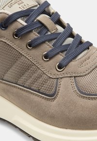 Sneaker in suede grigio con accenti in tessuto testurizzato, lacci blu navy, occhielli in metallo e suola in gomma crema. Presenta dettagli cuciti.