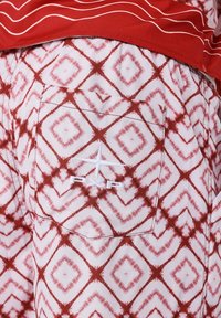 Rode en witte korte broek met diamanten patronen in een tie-dye stijl. Bevat een achterzak met een witte geborduurde logo.