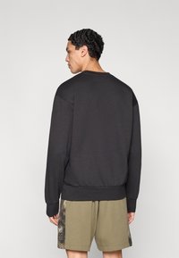 Melna džemperis ar garām piedurknēm, ribām piedurknēs un apakšmalā. Mīksta tekstūra un brīvs piegriezums, kopā ar olīvu zaļām šortām ar rakstainu maliņu.