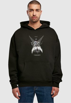 Schwarzer Baumwollhoodie mit einem grafischen Druck einer Statue mit Flügeln, vorderer Tasche und gerippten Bündchen. Das Modell steht in lässigen Jeans.