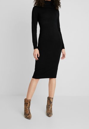 Black, long-sleeve, form-fitting dress with a mock neck, paired with tan and brown snake-patterned ankle boots. Smooth fabric texture.