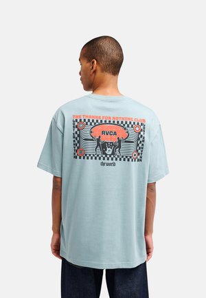 Uomo che indossa una maglietta azzurro chiaro con un design grafico con silhouette, testo e simboli sulla schiena.