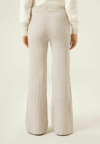 Jasnobeżowe, prążkowane, rozkloszowane spodnie dziane z wysokim, elastycznym pasem, z teksturowanym wzorem i dopasowaniem w talii.