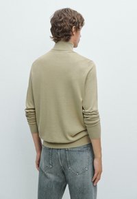 Ljust beige stickad tröja med hög krage och långa ärmar, i kombination med grå jeans. Passformen är avslappnad och framhäver den mjuka texturen och designen.