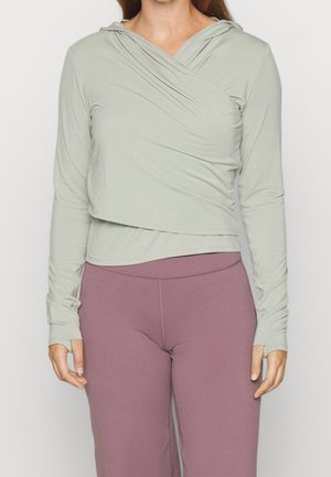 Jasnozielona bluza z długim rękawem ma powlekany design, miękką tkaninę i otwory na kciuki. W zestawie z fioletowymi legginsami o wysokim stanie.