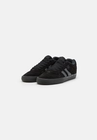 Black suede sneakers with gray accents, featuring a round toe, flat laces, and textured rubber sole. Two vertical stripes on the side.