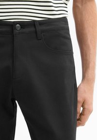 Zwarte katoenen broek met een rechte snit, voorzien van een voorzak, knoopsluiting en een gladde textuur. Gecombineerd met een gestreept shirt.