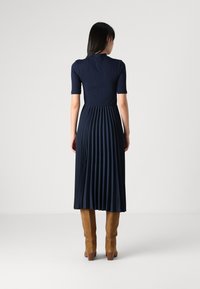 Jūras spēku kleita ar pieguļošu augšdaļu un krokotām svārkām. Īsas piedurknes, ribota tekstūra, līdz potītēm gara, apvienota ar brūnām ceļgala augstām zābakiem.