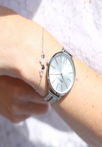 Edelstahl-Armbanduhr mit einem metallischen Mesh-Armband und einem minimalistischen Zifferblatt, kombiniert mit einem zarten Silberarmband mit funkelnden Akzenten.