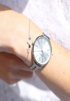 Zilveren polshorloge met een metalen meshband en een minimalistische wijzerplaat, vergezeld van een delicate zilveren armband met sprankelende accenten.
