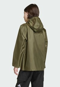 Olivovo zelená nepremokavá bunda s kapucňou, s hladkou, lesklou textúrou a elastickými manžetami, v kombinácii s čiernymi cargo nohavicami.