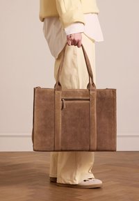 Bruine leren tote bag met twee lange handvatten, een voorzak met rits en een minimalistisch ontwerp. Gladde textuur en rechthoekige vorm.