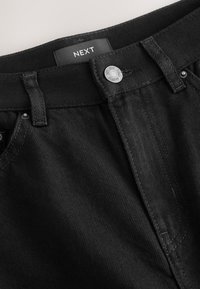 Sorte denimbukser med en tekstureret finish, der har en sølvknaplukning og mærket "NEXT" på linningen.