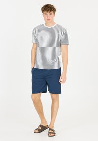 Witte en marineblauwe gestreepte t-shirt, marineblauwe shorts en bruine sandalen. T-shirt heeft een ronde hals en korte mouwen, shorts hebben een gladde textuur.