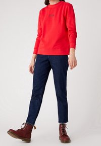 Sweatshirt rouge à col rond, avec des poignets et un ourlet côtelés ; assorti à un jean en denim foncé et des bottes lacées bordeaux.