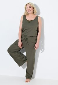 Olijfgroene, mouwloze jumpsuit met een V-hals en kantdetail. Heeft een taille met trekkoord en een wijd been ontwerp, gemaakt van zachte stof.