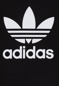T-shirt en coton noir avec un grand logo Adidas blanc comprenant trois formes de feuilles et trois bandes horizontales au-dessus du nom de la marque.