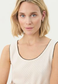 Light beige top with a textured pattern, wide scoop neckline, and black scalloped trim along the edges. No distinct hardware or accents.