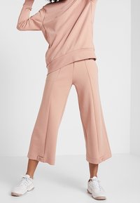 Sweatshirt rose clair et pantalon large coupé en tissu doux, avec une coupe décontractée et des poignets repliés. Stylisé avec des baskets blanches.