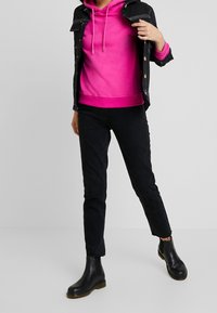 Černé džíny v kombinaci s živým růžovým sweatshirten a černou džínovou bundou. Vzhled doplňují zaprášené černé kotníkové boty.