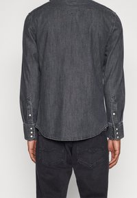 Tumman farkkukankaan paita pitkillä hihoilla, terävä yoke-yksityiskohta ja nappikahvat. Sisältää kaarevan helman ja vastakkaisesti ommeltuja yksityiskohtia.