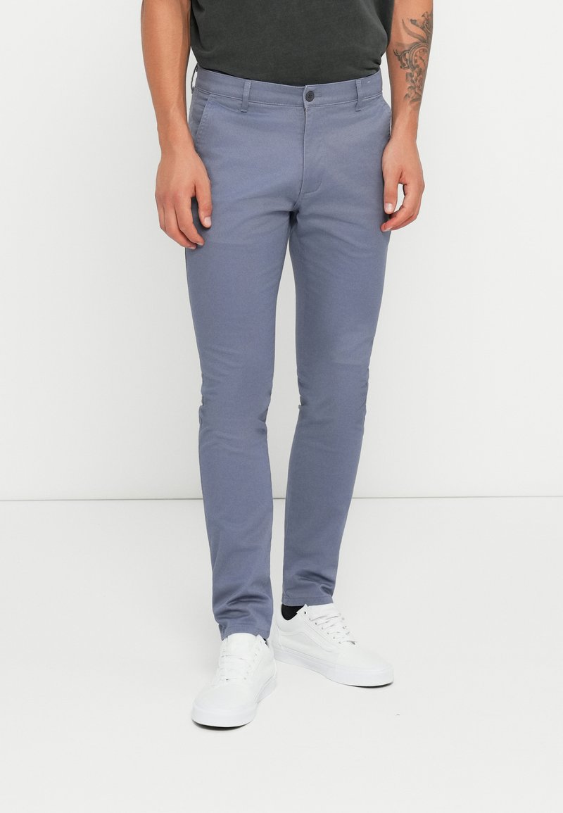 Lys grå slim-fit bukser med en glat tekstur, med en frontknap, bælteløkker og sidelommer, parret med hvide sneakers.