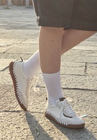 Bijele teniske od platna, s smeškim gumenim đonovima, teksturiranim bočnim detaljima i belim vezicama, uparene s belim čarapama do članka.