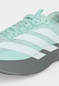 Basket Adidas bleu clair avec des rayures blanches, des lacets texturés et une semelle épaisse gris foncé, vue de côté avant.